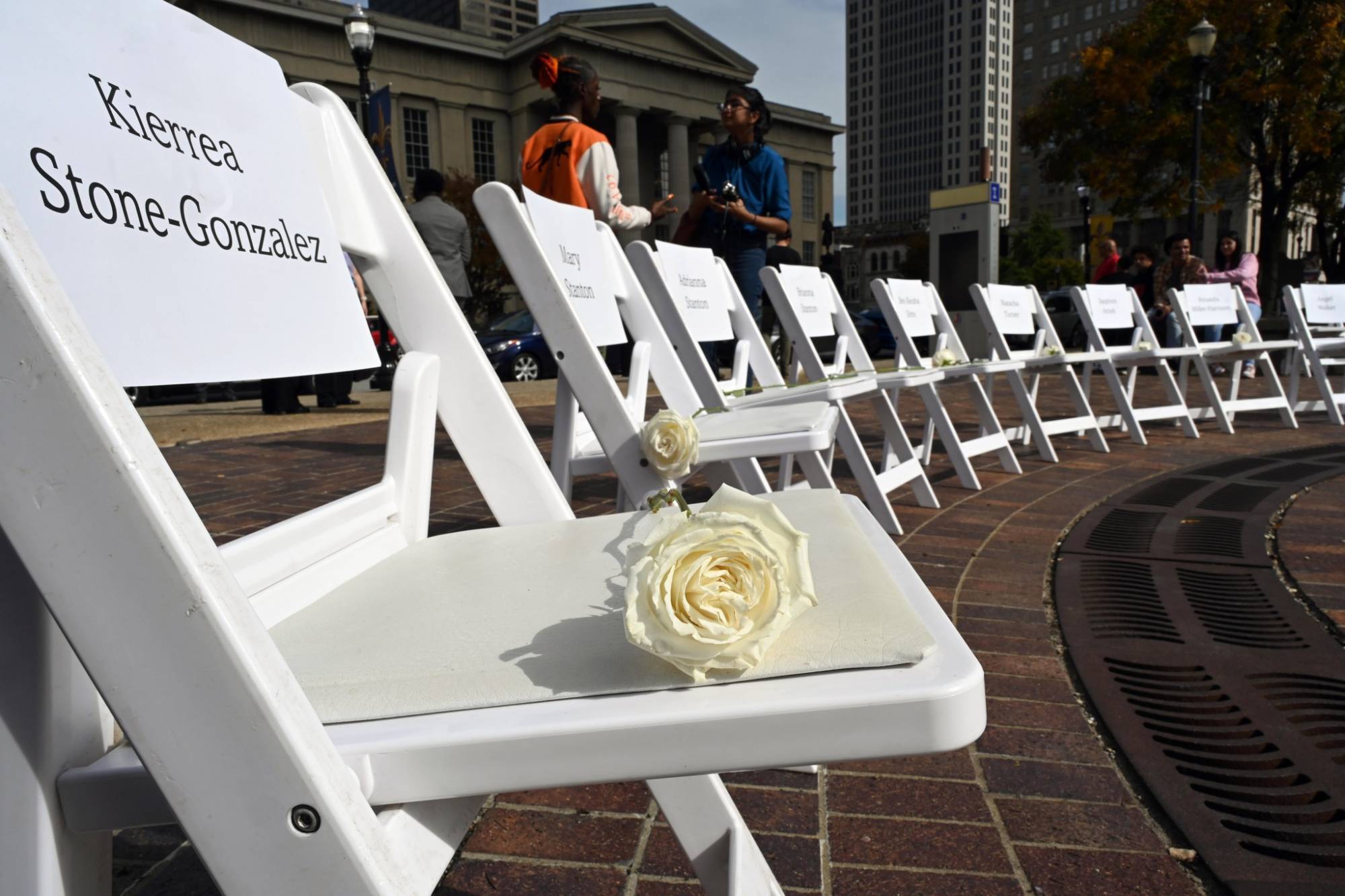 Photo of white chairs that were placed in Jefferson Square Park during The Center's Speak Their Names ceremony October 24 to honor the memory of victims who lost their lives to domestic violence in 2023. A rose was placed on each chair as the victims' names were read during the event.